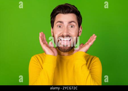 Photo de l'homme impressionné avec la barbe élégante habillée chemise jaune soulevant des paumes sur le visage étonné regardant isolé sur fond de couleur verte Banque D'Images