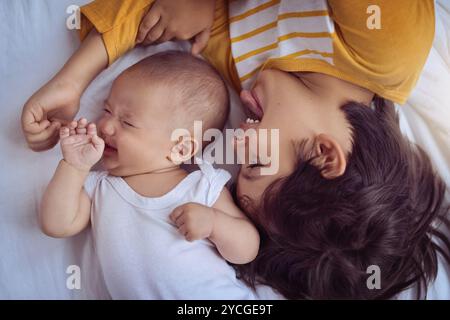 Bébé, frère et jouer sur le lit à la maison avec du bruit, pleurs et nouveau-né agacé dans la chambre. Vue de dessus, les gens ou le nourrisson hurlant dans la pépinière avec Banque D'Images