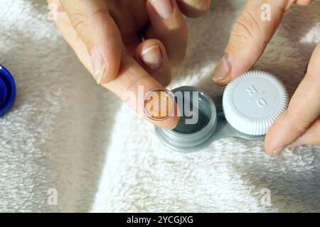 Une lentille de contact brune posée sur l'index. Porter des lentilles de contact colorées : une femme sort une lentille d'un récipient pour l'insérer dans son œil Banque D'Images