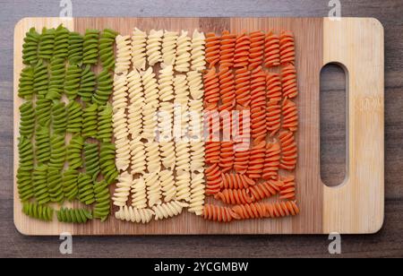 Spirales, spirelli ou fussili pâtes tricolores nouilles dans les couleurs nationales italiennes, vert, blanc, rouge sur une planche de cuisine en bambou Banque D'Images