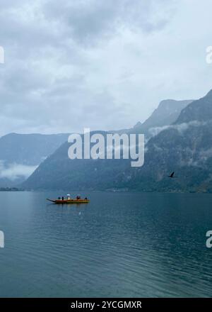 Hallstatt, Autriche - 2 octobre 2024 : couple se marie sur un bateau en bois sous la pluie sur le lac Hallstatt, entouré par les Alpes brumeuses un jour nuageux Banque D'Images