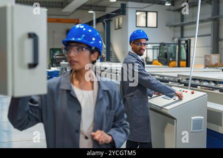 Deux ingénieurs d'usine, une indienne et un afro-américain, surveillent les panneaux de commande et le processus de fabrication automatisé. Banque D'Images