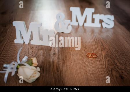 Symboles de mariage élégants avec anneaux et accent floral sur plancher en bois. Banque D'Images