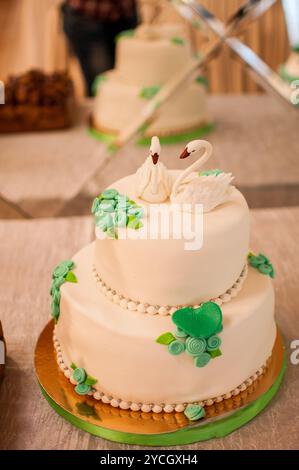 Elégant gâteau de mariage à deux niveaux avec des toppers de cygne et des accents floraux. Banque D'Images