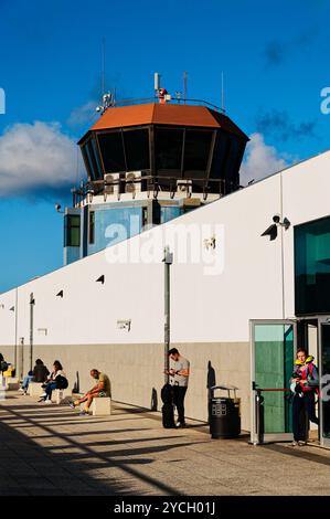 Les voyageurs se détendent à l'extérieur du terminal sous la tour de contrôle de l'aéroport de Funchal, en profitant du soleil de l'après-midi avant leurs vols Banque D'Images