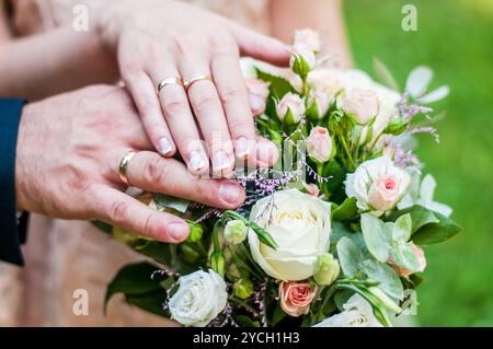 Bouquet de mariage romantique avec des mains entrelacées et des anneaux dans un cadre de jardin luxuriant. Banque D'Images