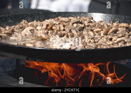 Les champignons grésillants cuisent dans une grande casserole au-dessus d'un feu ouvert Banque D'Images