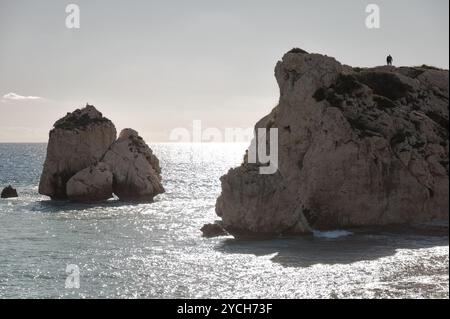 Couple est debout sur une falaise, admirant le magnifique coucher de soleil sur la mer Méditerranée avec le rocher d'Aphrodite (Petra tou Romiou) en arrière-plan. PA Banque D'Images