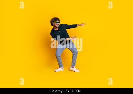 Jeune homme en chemise noire et jeans pose ludique sur fond jaune Banque D'Images