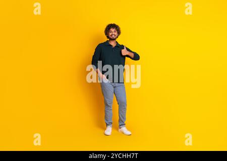 Un jeune homme portant une chemise noire et un Jean donne un pouce vers le haut sur un fond jaune vif, mettant en valeur une attitude joyeuse et positive Banque D'Images