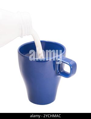 Verser le lait de la bouteille dans la tasse bleue Banque D'Images