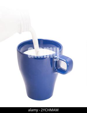 Verser le lait de la bouteille dans la tasse bleue Banque D'Images