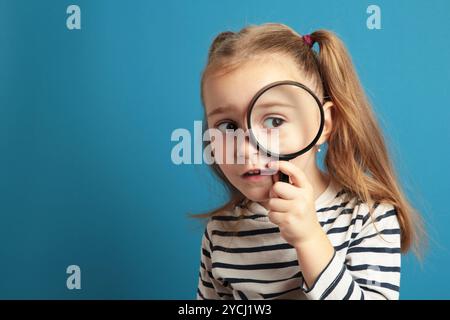 Petite fille enfant regardant à travers une loupe sur fond bleu. Vue de dessus Banque D'Images