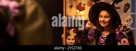 Bannière de jolie fille joyeuse en costume de sorcière d'Halloween debout devant le miroir tout en se préparant pour la fête contre le garçon démon Banque D'Images