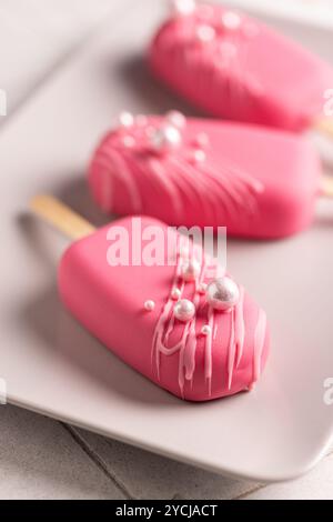 Glace végétalienne sur un bâton en glaçage framboise, décorée de perles comestibles, un régal pour la Saint-Valentin, anniversaire Banque D'Images