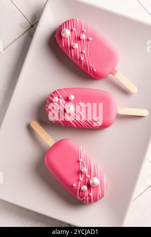 Glace végétalienne sur un bâton en glaçage framboise, décorée de perles comestibles, un régal pour la Saint-Valentin, anniversaire Banque D'Images