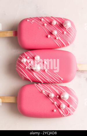 Glace végétalienne sur un bâton en glaçage framboise, décorée de perles comestibles, un régal pour la Saint-Valentin, anniversaire Banque D'Images