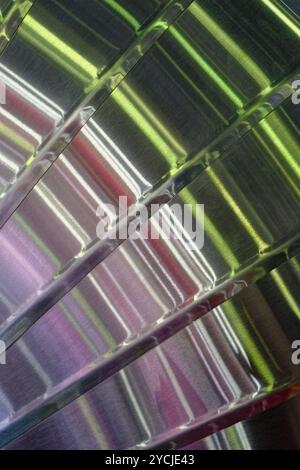 Reflets lumineux multicolores sur une surface courbe en acier inoxydable brossé, fond industriel abstrait Banque D'Images