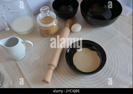 Ingrédients de cuisson pour cuire des petits pains sucrés, levure dans des plats de bol noir avec rouleau à pâtisserie sur une table Banque D'Images