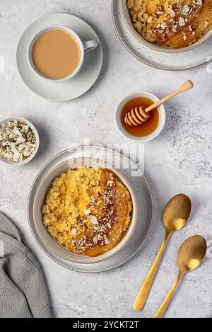 Photographie alimentaire de bouillie de millet avec banane caramélisée, noix de pécan, noix, flocons de noix de coco, chia, graines de lin, miel, thé au lait d'amande Banque D'Images