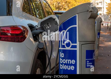 Gros plan d'une voiture électrique branchée pour être rechargée à une borne de recharge appartenant au réseau français la borne bleue, Nanterre, France Banque D'Images
