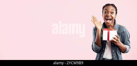 Joyeuse Dame africaine criant tenant cadeau posant sur fond rose Banque D'Images