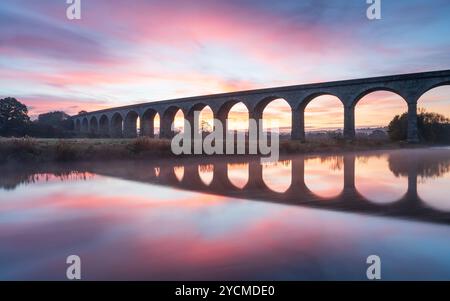 Un magnifique lever de soleil d'automne encadre les arches distinctives du viaduc d'Arthington, reflétées dans la rivière Wharfe par un matin d'octobre froid. Banque D'Images