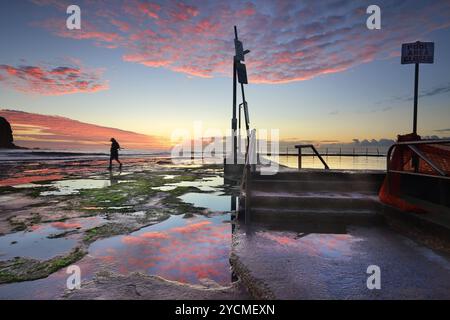 Lever de soleil sur les rochers près de la piscine à Mona Vale, Northern Beaches, Sydney, un ciel fantastique et la silhouette d'un pêcheur en mouvement. Banque D'Images