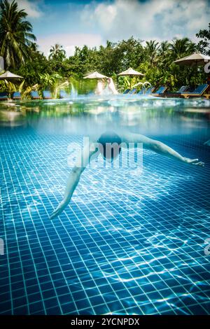 L'homme plonge dans une piscine donne sur l'eau et sous l'eau. Les Maldives. Banque D'Images