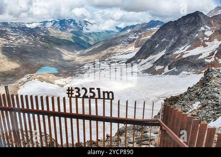 Panneau rouillé indiquant l'altitude de 3251 mètres au-dessus du niveau de la mer au glacier Schnalstal dans le Tyrol du Sud, Italie, avec un lac en arrière-plan Banque D'Images