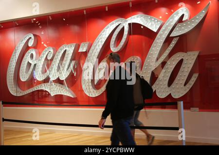 Atlanta, États-Unis. 23 octobre 2024. Les visiteurs passent devant un logo Coca-Cola au World of Coca-Cola à Atlanta, en Géorgie, aux États-Unis, le 23 octobre 2024. Les actions de Coca-Cola ont chuté de près de 2 % mercredi après que la société ait annoncé des volumes de cas unitaires plus faibles que prévu au troisième trimestre. Crédit : Liu Yanan/Xinhua/Alamy Live News Banque D'Images