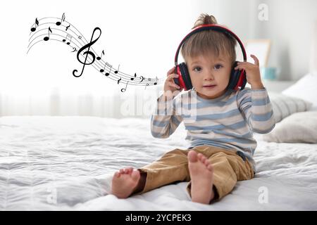 Mignon petit bébé dans des écouteurs sur le lit à la maison. Notes de musique volant près de l'enfant Banque D'Images