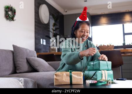 Emballage de cadeaux de Noël à la maison, femme senior asiatique souriant pendant les préparatifs des vacances Banque D'Images