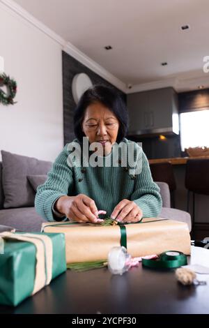 Femme âgée senior asiatique enveloppant des cadeaux de Noël à la maison, en se concentrant sur les détails Banque D'Images