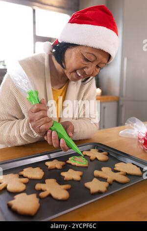 Décorer des biscuits de Noël, femme senior asiatique souriant tout en cuisinant les vacances à la maison Banque D'Images