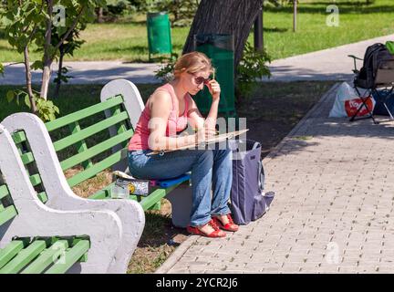 La jeune fille attire l'assis sur un banc dans un parc de la ville Banque D'Images