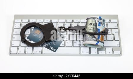 Menottes en acier, carte de crédit et billet de dollars couché sur un clavier d'ordinateur sur le fond blanc Banque D'Images