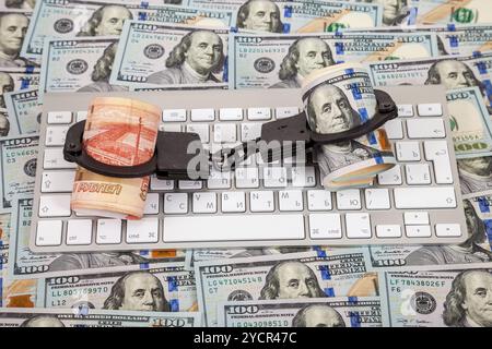 Menottes en acier, rouleaux de roubles russes et dollars couchés sur un clavier d'ordinateur sur fond de dollars Banque D'Images