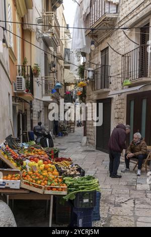 Bari, Italie, 27 novembre 2023 : Greengrocer dans une ruelle étroite de la vieille ville de Bari discutant avec un client, Europe Banque D'Images