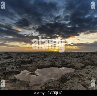 Coucher de soleil idyllique sur une plage rocheuse sur le golfe de Tarente dans les Pouilles avec un bassin de marée au premier plan Banque D'Images