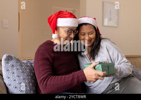 Noël, couple multiracial senior souriant dans les chapeaux de père noël échangeant des cadeaux Banque D'Images