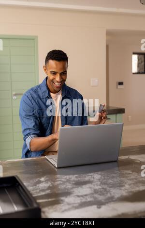 Souriant afraican homme américain utilisant un ordinateur portable et tenant la carte de crédit à la maison pour les achats en ligne Banque D'Images