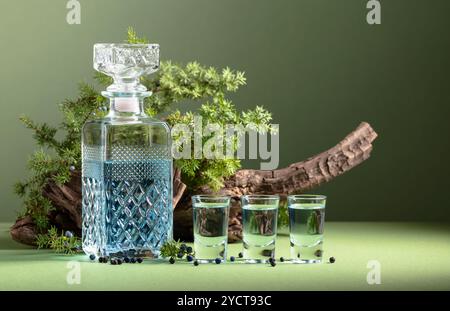 Gin bleu en carafe sur un fond de vieux accrocs et de branches de genévrier avec des baies. Fond vert avec espace de copie. Banque D'Images