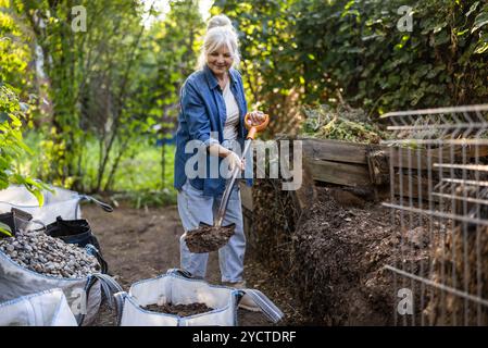 Femme âgée pelletant un tas de compost dans son jardin Banque D'Images