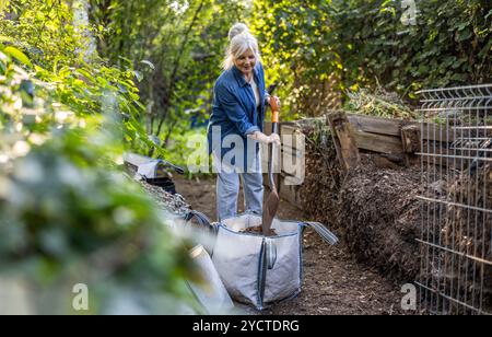 Femme âgée pelletant un tas de compost dans son jardin Banque D'Images