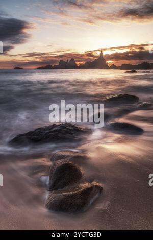 Phare du Corbière au coucher du soleil à marée basse. Vagues et pierres sur la plage. Banque D'Images