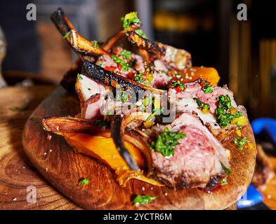 Côtelettes d'agneau parfaitement grillées sur une planche de bois, accompagnées de légumes frais et garnies d'herbes, prêtes à servir. Banque D'Images