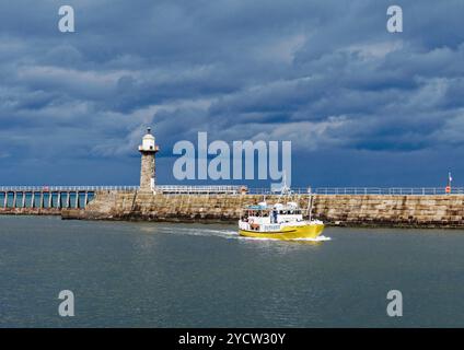 Whitby, North Yorkshire avec un bateau d'excursion plus petit donnant des excursions touristiques le long de la côte entre dans le port avec la pierre East Pier derrière. Banque D'Images