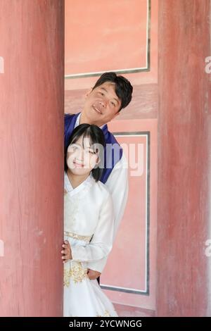 Un couple coréen, un homme dans ses 30 ans et une femme dans ses 20 ans, porte heureusement Hanbok et jette un coup d’œil depuis un pilier dans un bâtiment historique à Séoul, dans le sud de Ko Banque D'Images