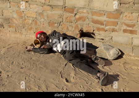 Vieil homme africain dormant sur un chemin de terre dans la ville, village, alcoolisme et toxicomanie Banque D'Images